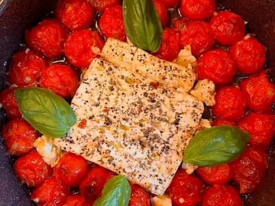 A baking dish with a softened block of feta surrounded by blistered cherry tomatoes, being stirred into a creamy sauce