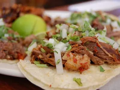 Griddled quesabirria tacos with melted cheese and shredded beef, served with a cup of red consomme for dipping