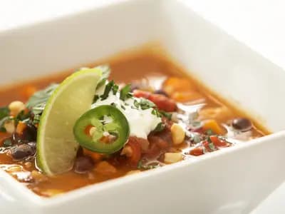 A steaming bowl of black bean sweet potato chili topped with sliced avocado, cilantro, and diced red onion