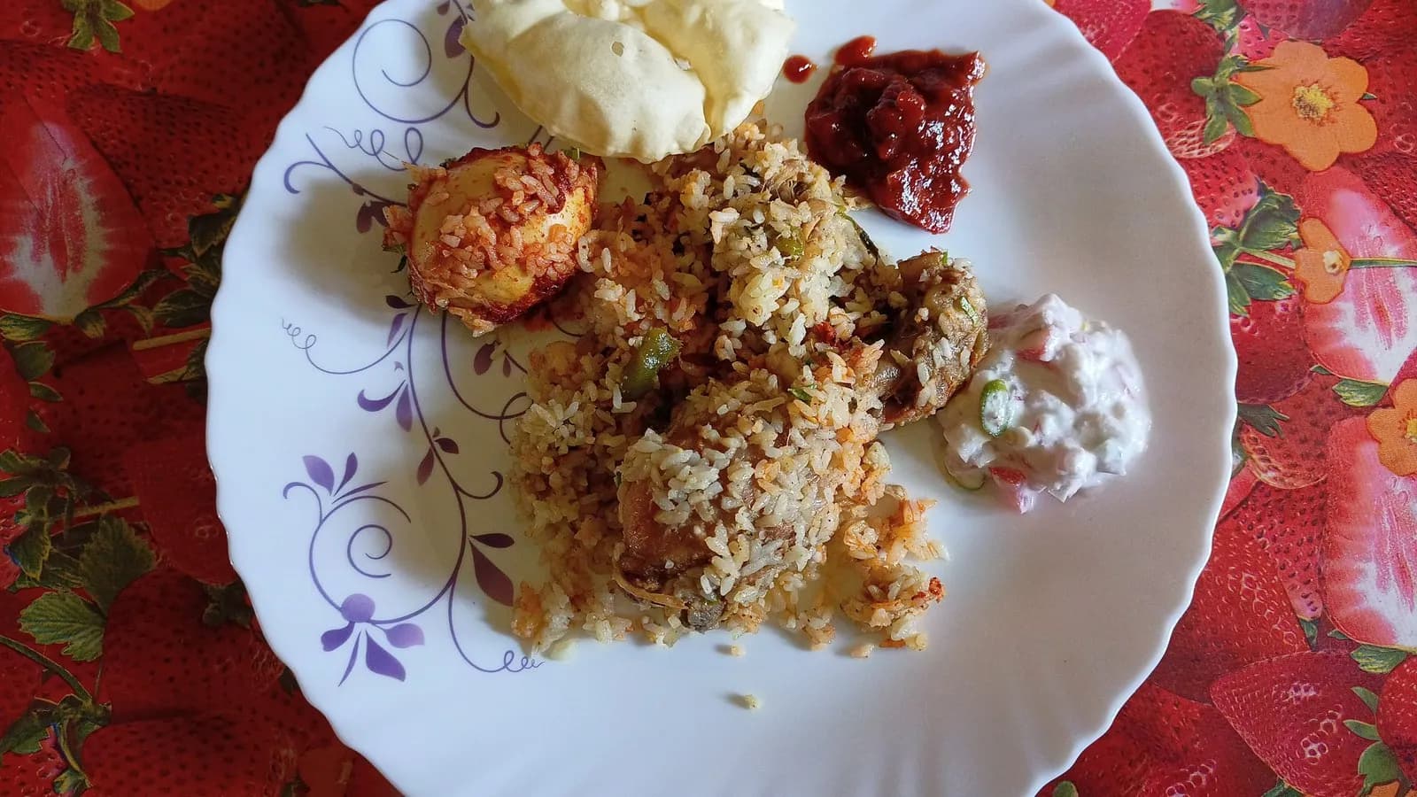 A plate of chicken biryani served with raita, a spoonful of pickle and a papad