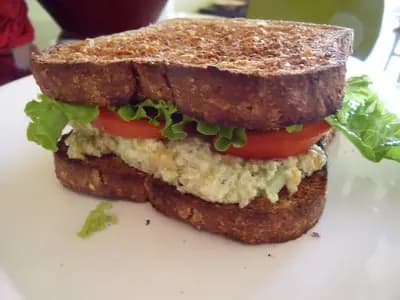 A generous scoop of chickpea salad on whole grain bread with dill and lemon garnish