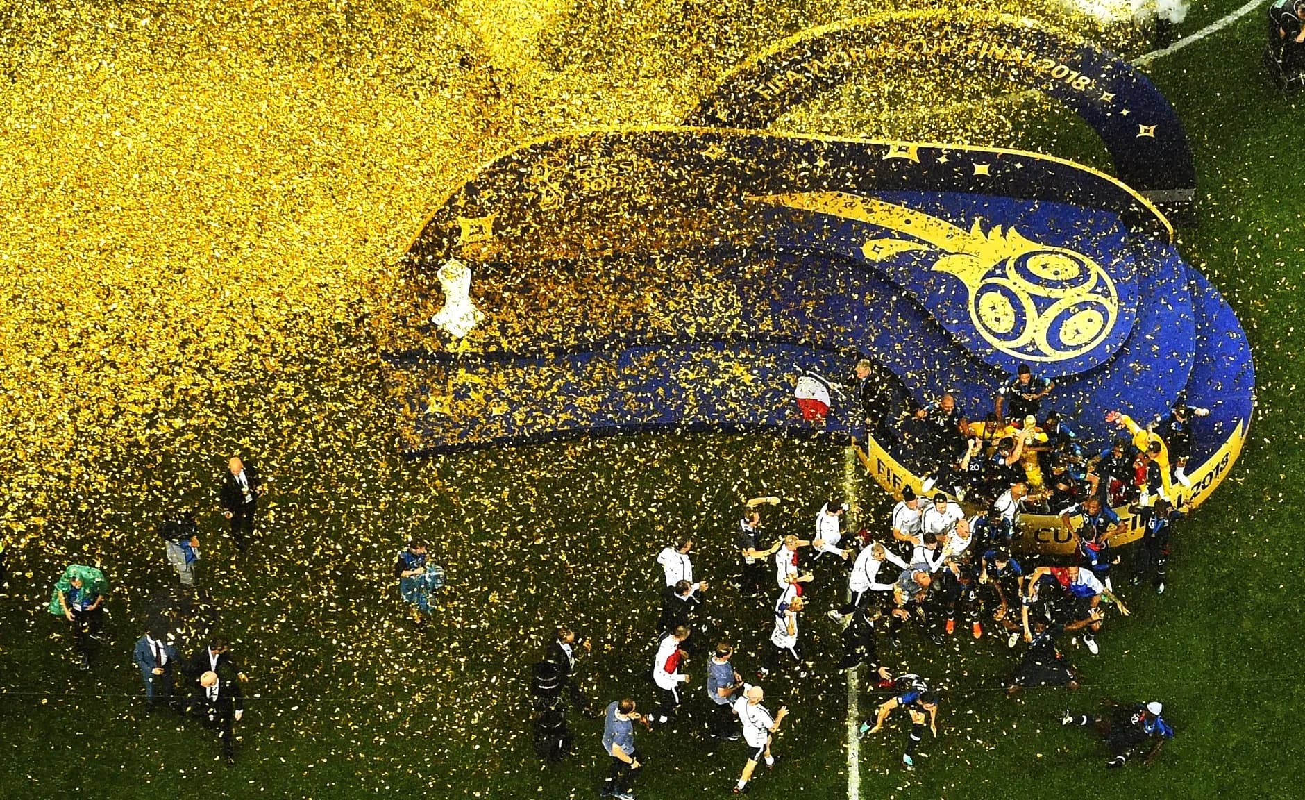 Football players in blue kits celebrating with a trophy on a stadium pitch surrounded by confetti
