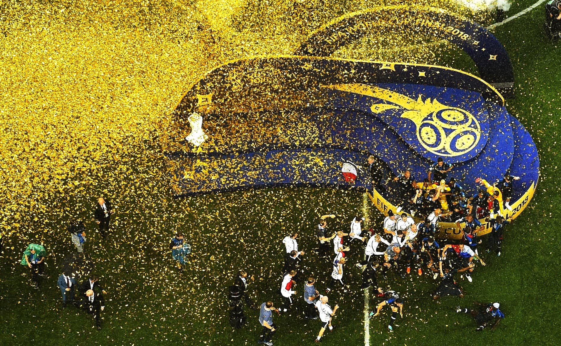 Football players in blue kits celebrating with a trophy on a stadium pitch surrounded by confetti