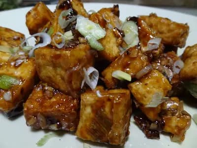 Golden-brown crispy tofu cubes glistening with peanut sauce, served over rice with cucumber slices