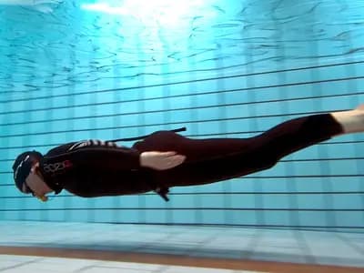 Divers descending through clear water in a deep indoor pool
