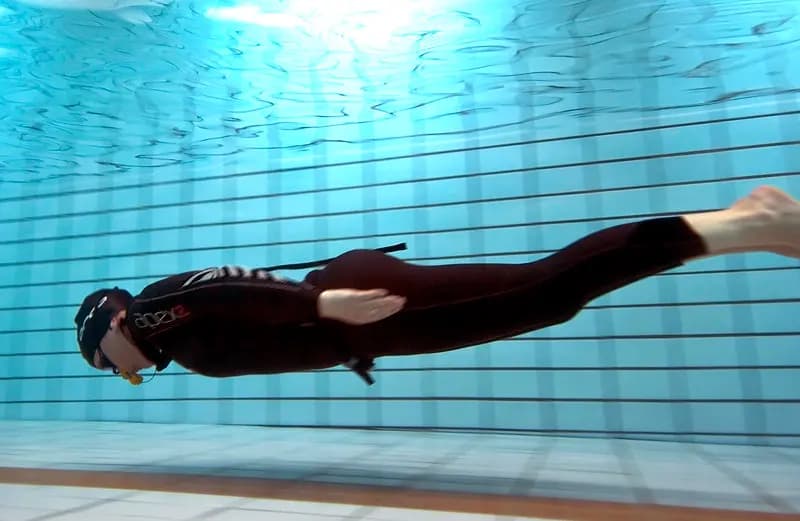 Divers descending through clear water in a deep indoor pool