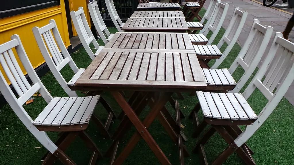 Empty wooden tables and chairs set out on the pavement outside a cafe