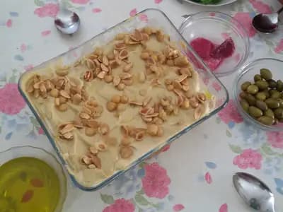 A wide dish of chickpeas and crisp pita under garlic yoghurt, topped with toasted pine nuts