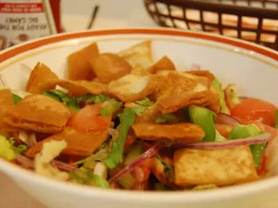 A vibrant bowl of fattoush salad with lettuce, tomatoes, cucumbers, and golden pita chips