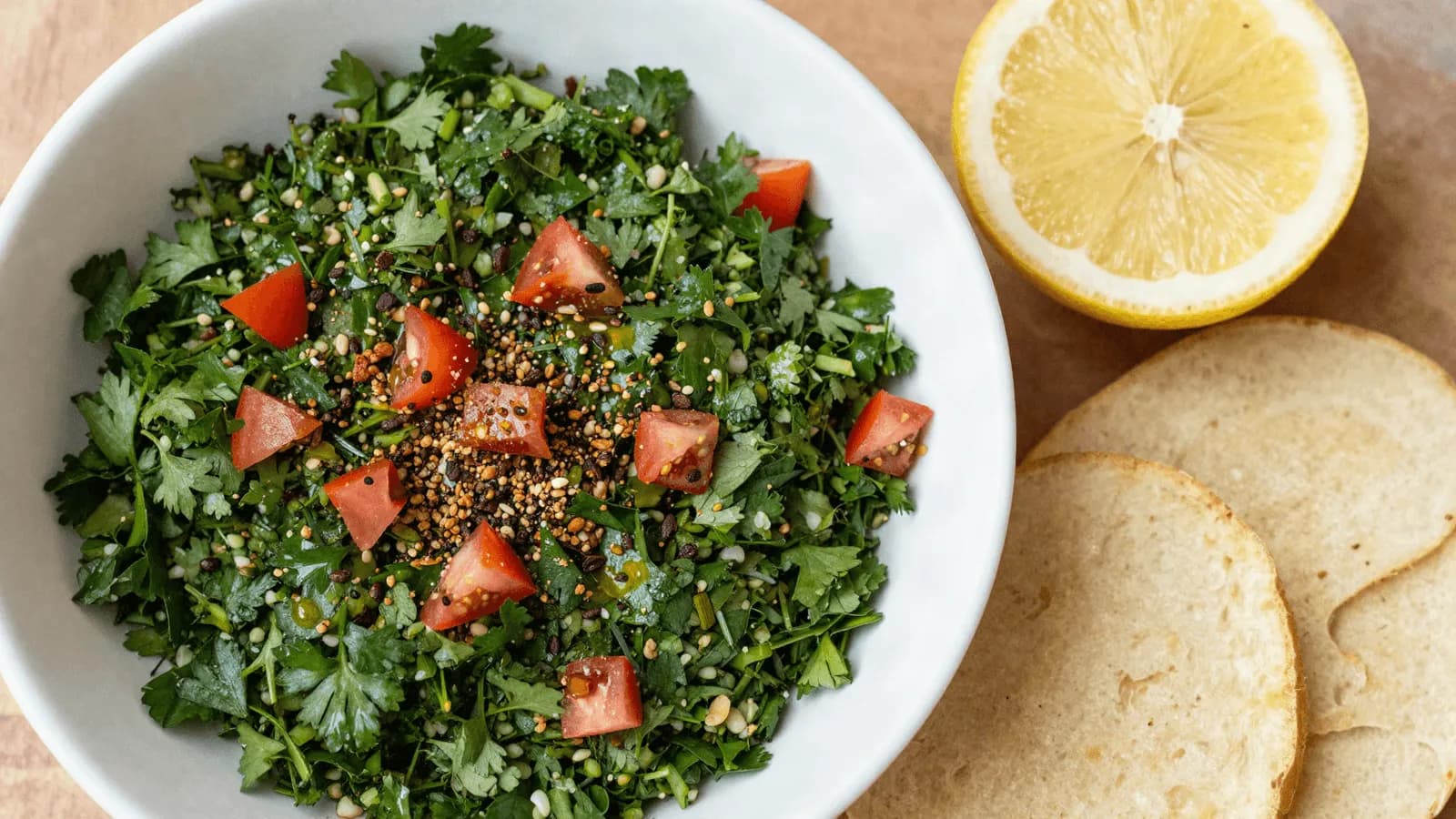 A bowl of bright green parsley tabbouleh with diced tomato and grains visible through it