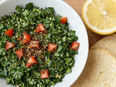 A bowl of bright green parsley tabbouleh with diced tomato and grains visible through it