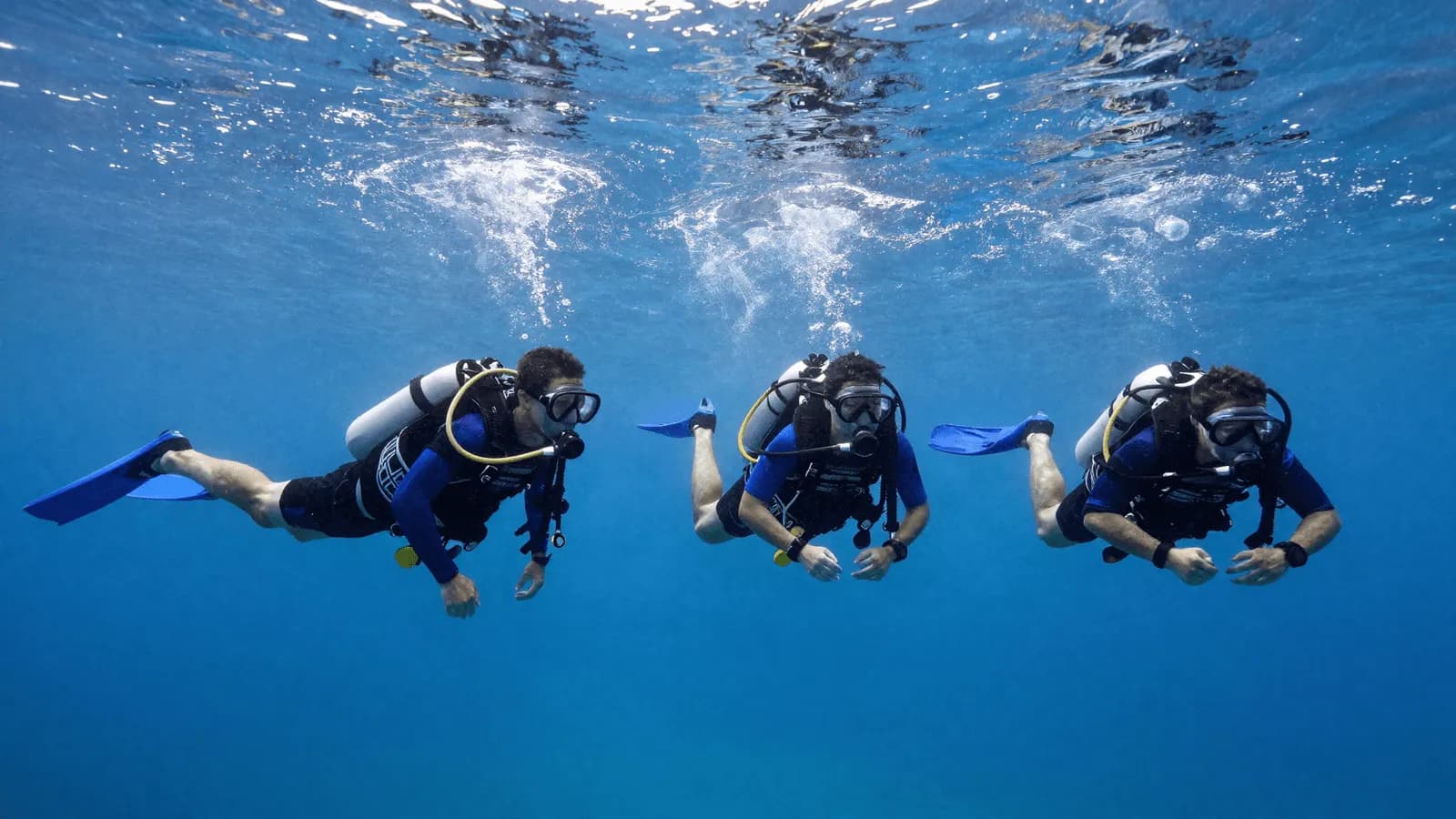 A team of divers holding horizontal trim together in mid-water, lights pointed forward