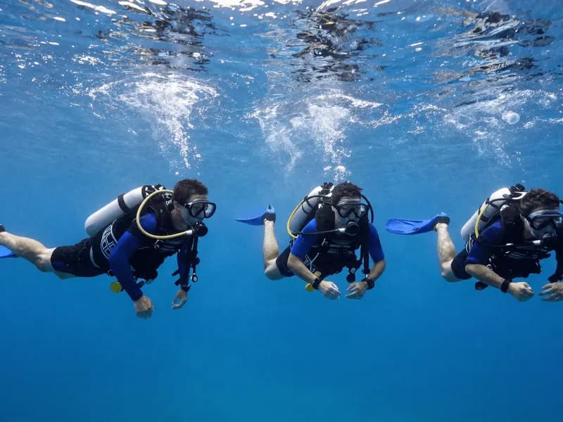 A team of divers holding horizontal trim together in mid-water, lights pointed forward