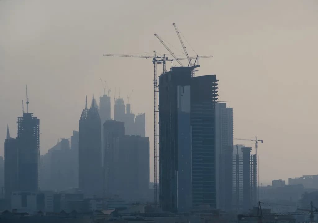 Construction cranes rising over a Gulf city skyline
