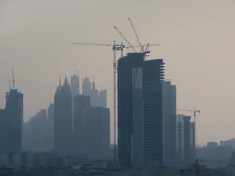 Construction cranes rising over a Gulf city skyline