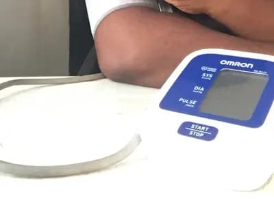 An automatic upper-arm home blood pressure monitor on a table beside a person's bare arm, photographed in April 2024