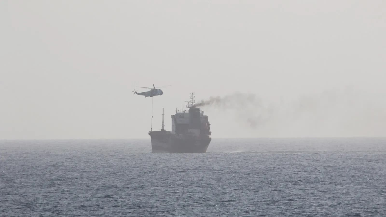 A merchant tanker under way in the Arabian Gulf while a helicopter lowers a boarding party onto its deck. The photograph records the boarding of the MT Wila in August 2020 and is not from the current closure