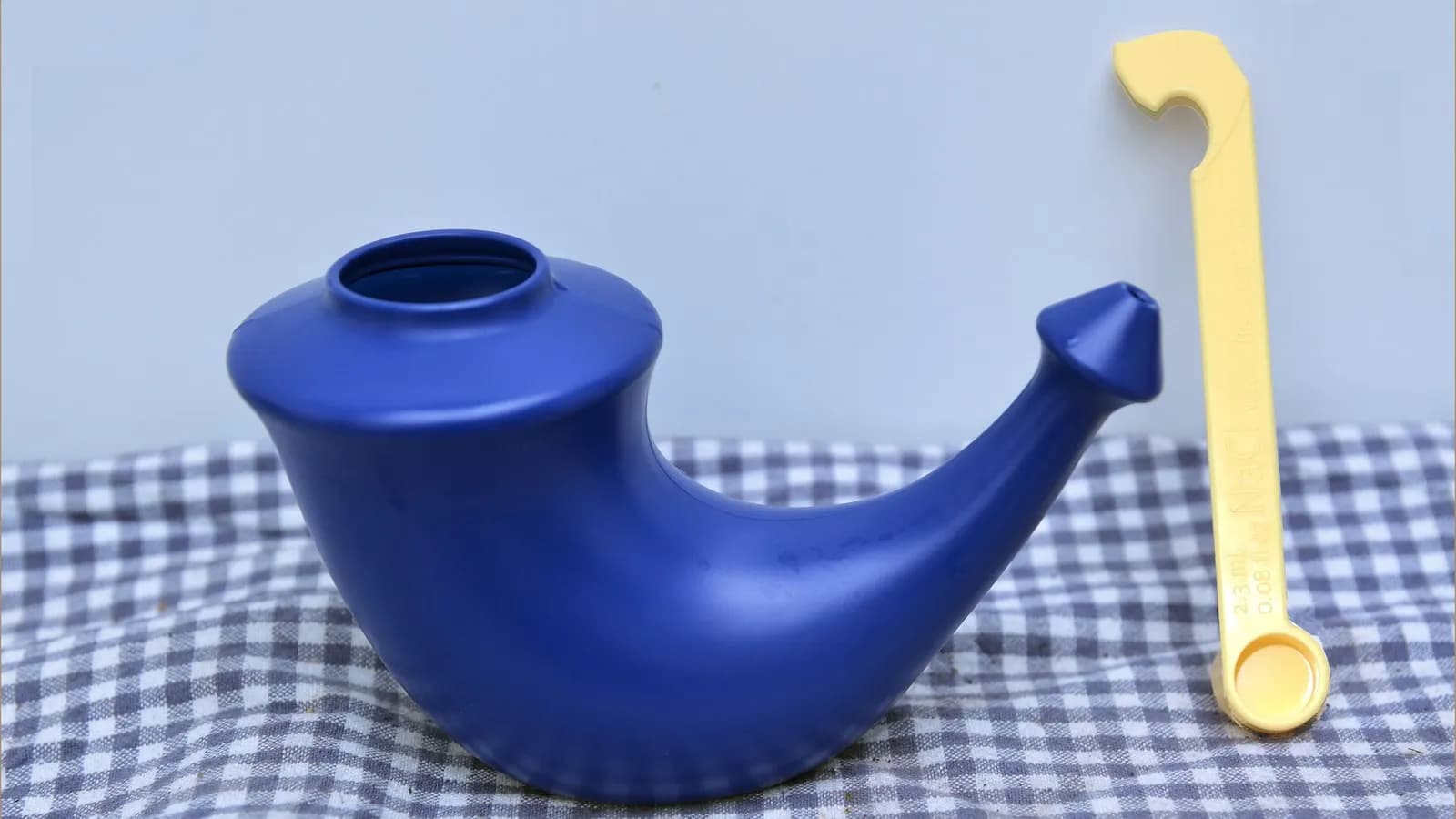 A blue ceramic neti pot with its measuring spoon, the shape used for pouring saline through one nostril and out of the other