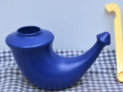 A blue ceramic neti pot with its measuring spoon, the shape used for pouring saline through one nostril and out of the other