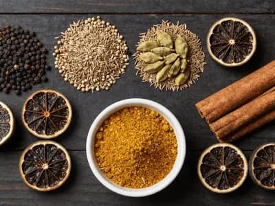 Whole spices and dried black limes beside a bowl of freshly ground kabsa blend