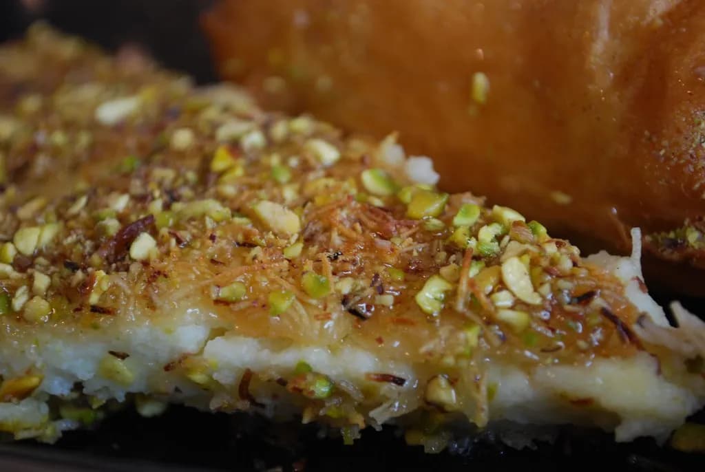 A golden knafeh dessert with melting cheese visible at the edges and crushed pistachios on top