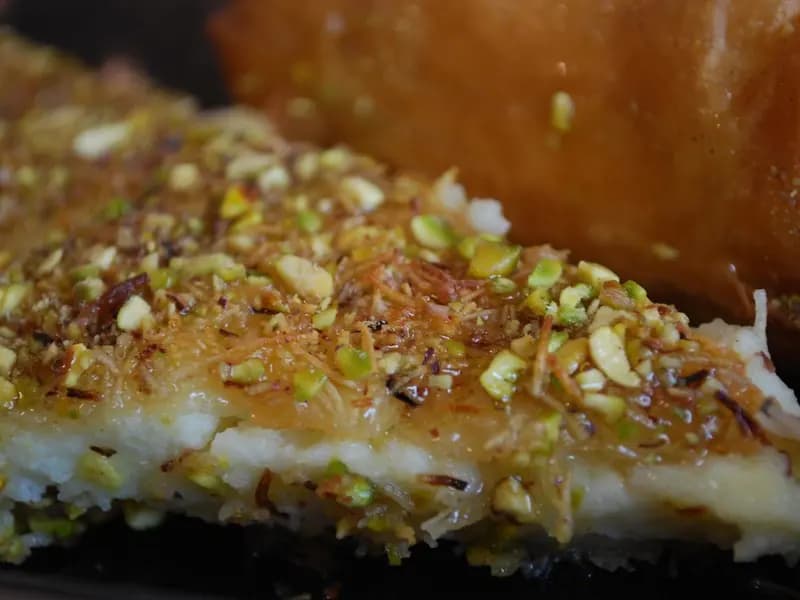 A golden knafeh dessert with melting cheese visible at the edges and crushed pistachios on top