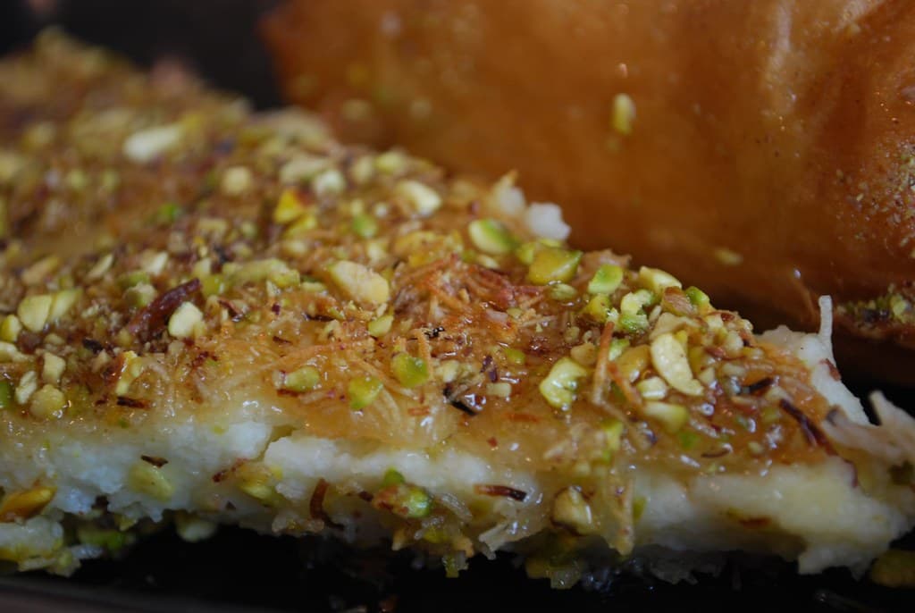 A golden knafeh dessert with melting cheese visible at the edges and crushed pistachios on top