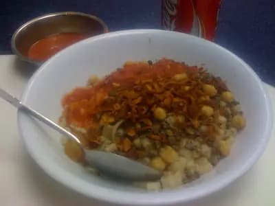 Bowl of koshari with layers of rice, lentils, elbow pasta, fried onions, tomato sauce, and dukka sauce with fresh cilantro garnish