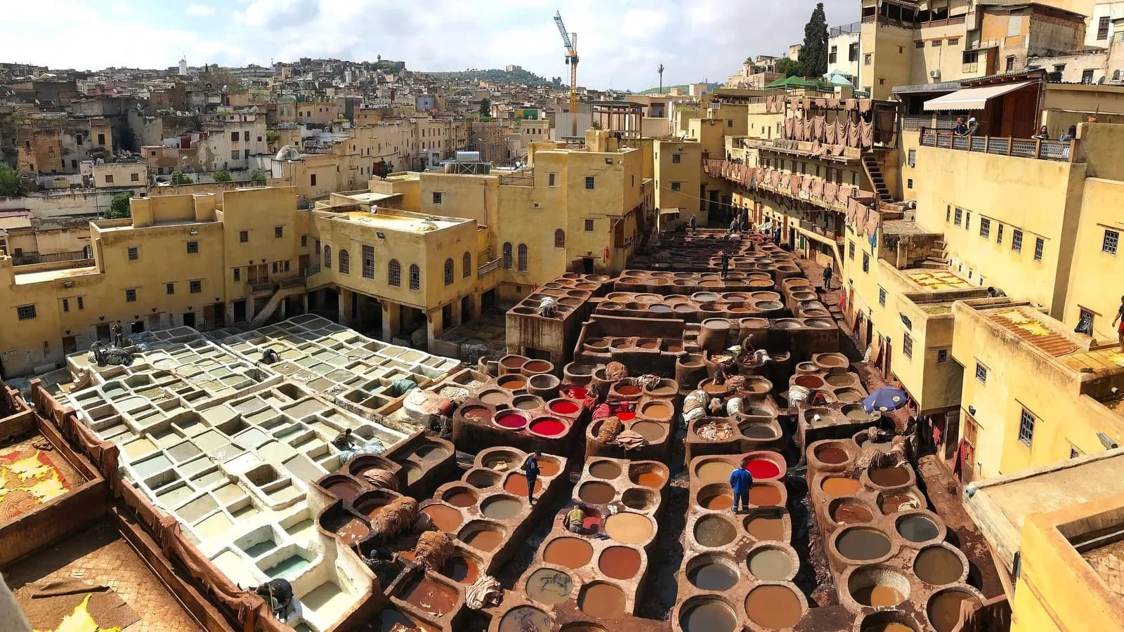 The stone vats of the Chouara tannery in Fez, filled with dye and tanning liquor, seen from the terraces above with the medina beyond