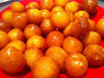A plate of small round golden fried dumplings glazed with dark date syrup and sesame seeds