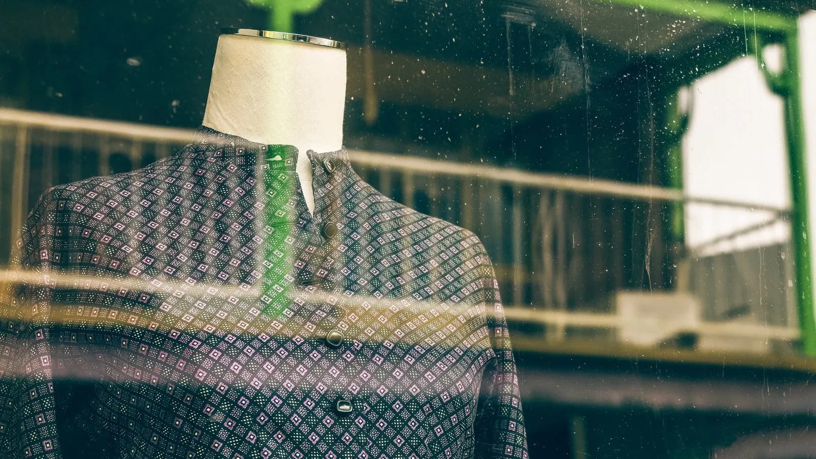 A mannequin in a jacket seen through a shop window, with the street reflected in the glass
