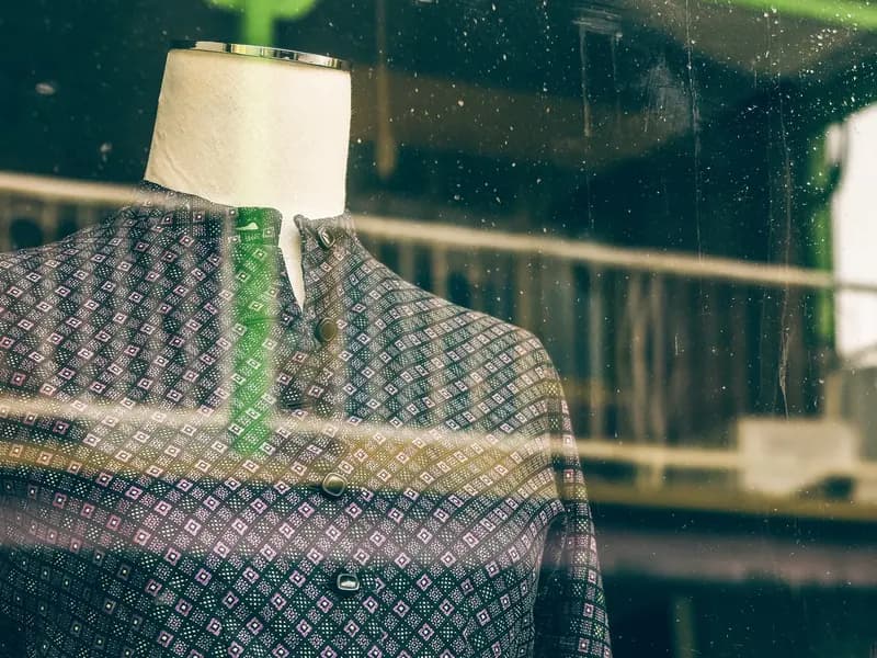 A mannequin in a jacket seen through a shop window, with the street reflected in the glass