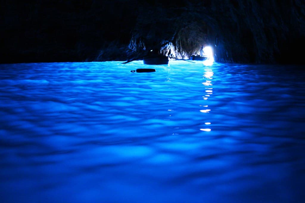 A technical diver silhouetted at the entrance of a deep underwater cave, lit by a dive torch