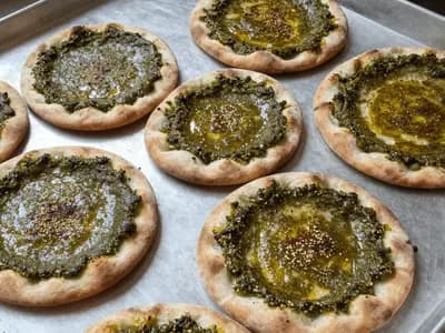 Round za'atar flatbreads fresh from the oven, the dark green herb paste glossy across the dimpled dough