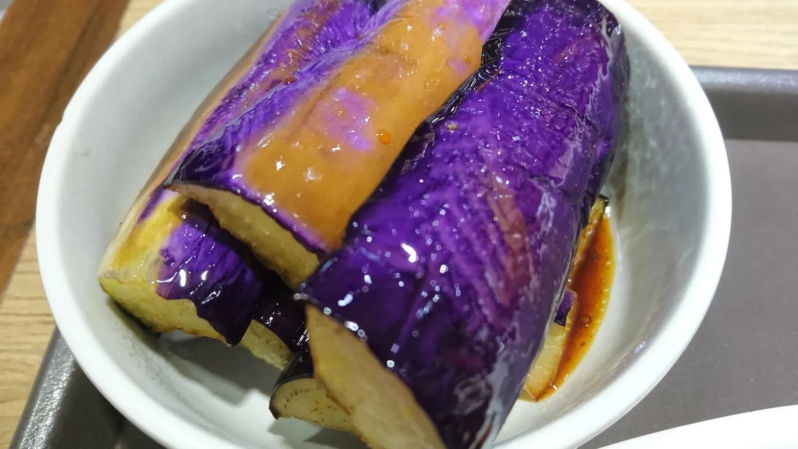 Japanese style grilled aubergine in a shallow bowl, the skin deep purple and the flesh collapsed and glossy under a dark sauce