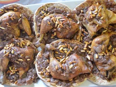 Roast chicken pieces on flatbread piled with dark red sumac onions and pine nuts