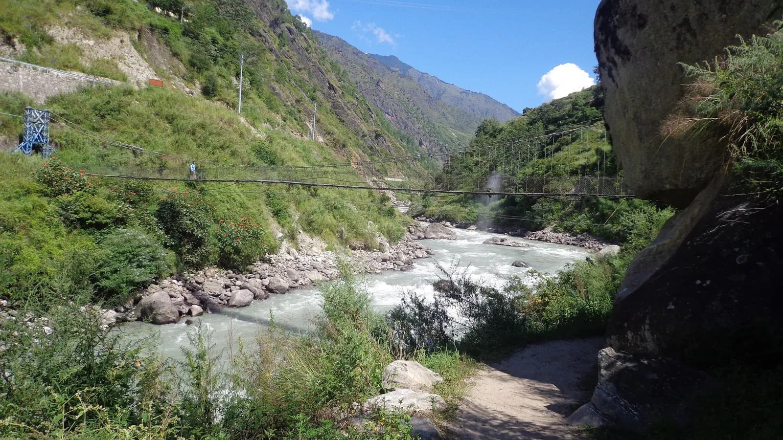 The Trishuli river running fast through a steep, narrow Himalayan valley in Nepal, with a footbridge crossing it
