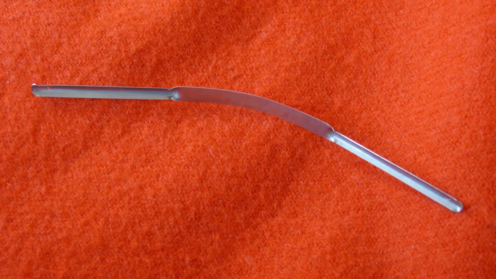 A stainless steel tongue scraper, the curved blade drawn from the back of the tongue forwards