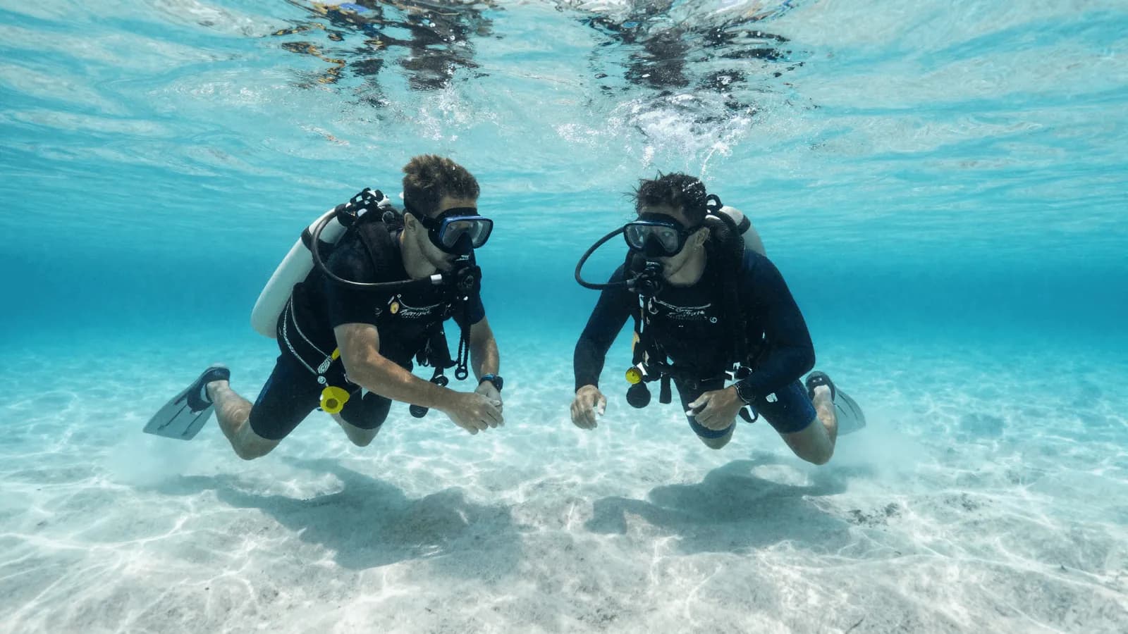An instructor guiding a student diver through a skill in clear shallow water
