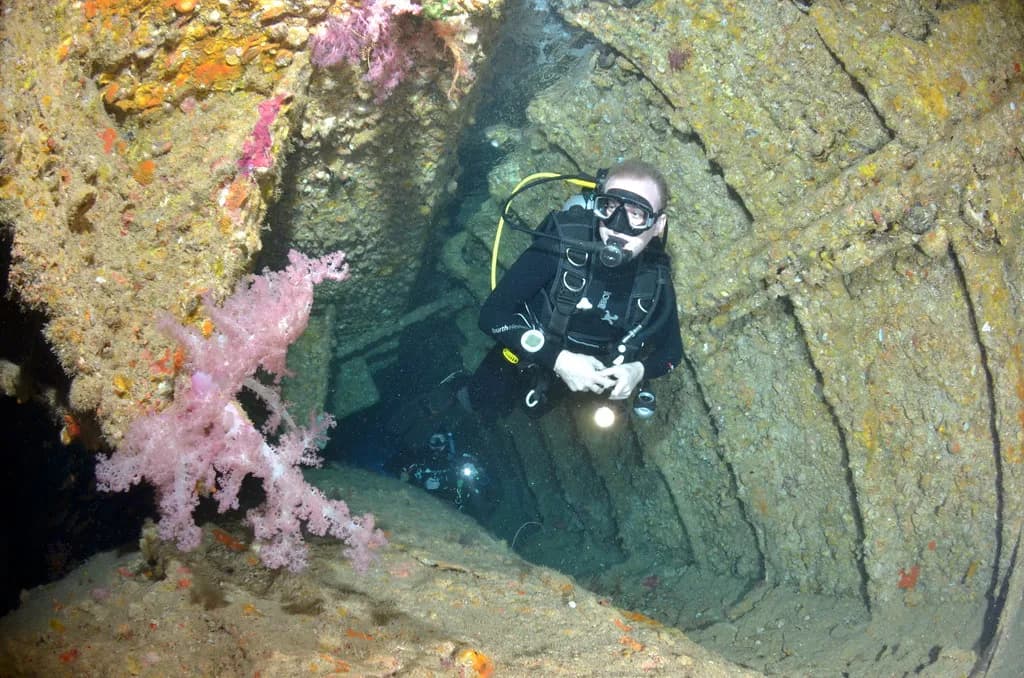 A technical diver equipped with staged cylinders preparing to descend near a wreck