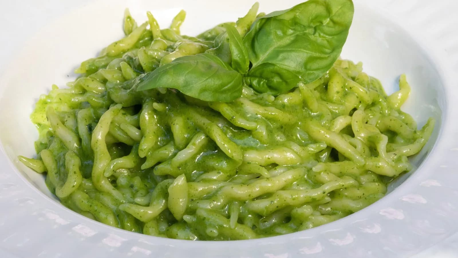 A plate of trofie al pesto, the short twisted Ligurian pasta coated in bright green pesto alla genovese and topped with a basil leaf