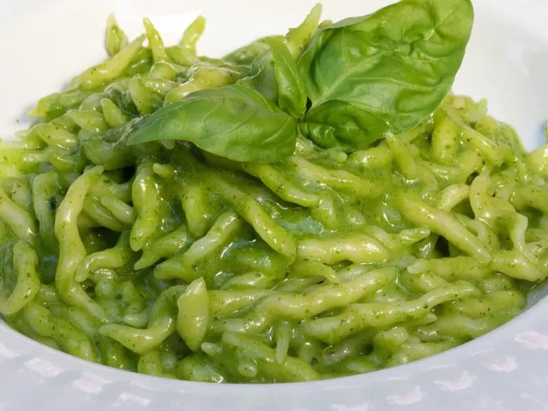 A plate of trofie al pesto, the short twisted Ligurian pasta coated in bright green pesto alla genovese and topped with a basil leaf