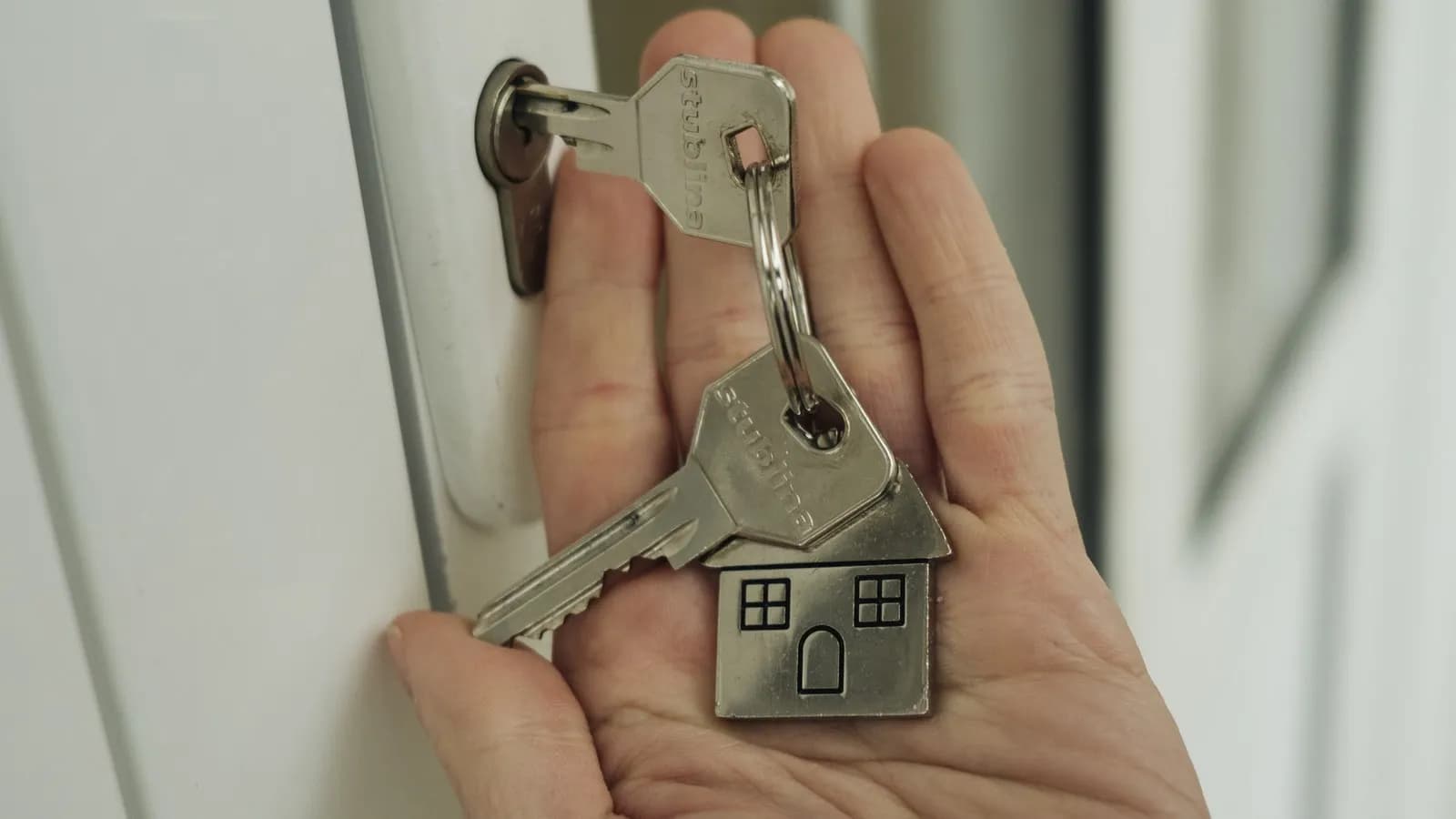 A hand holding a set of house keys on a house shaped fob, raised to a door lock