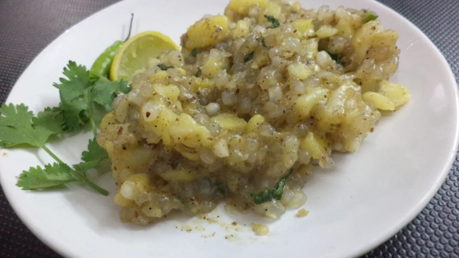 A plate of sabudana khichdi, the tapioca pearls translucent and separate rather than clumped, finished with coriander and lime