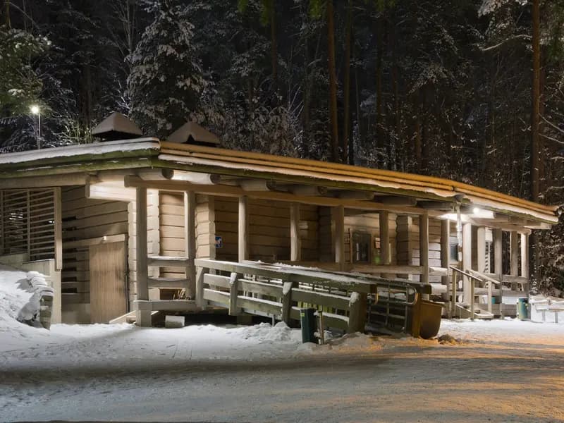 The public smoke sauna at Kuusijärvi in Vantaa, Finland, its timber walls lit at night with snow on the ground and the forest behind
