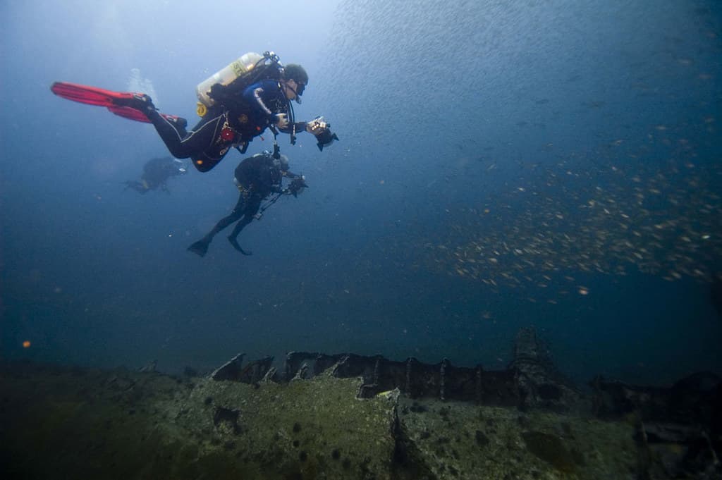 A marine researcher in scuba gear conducting an underwater reef survey with a slate and camera