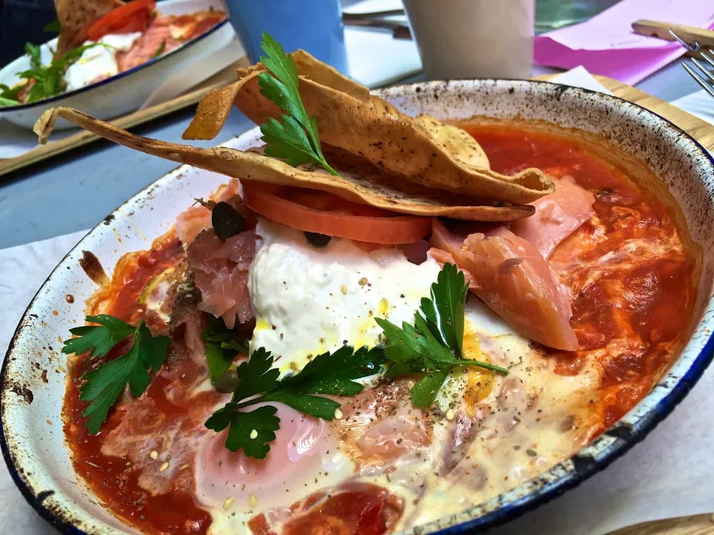 Cast iron skillet of shakshuka with poached eggs in spiced tomato sauce, garnished with fresh cilantro and crumbled feta cheese