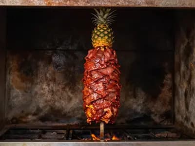 A vertical trompo of red marinated pork with a pineapple fixed on top