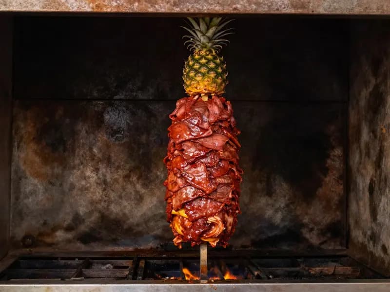 A vertical trompo of red marinated pork with a pineapple fixed on top