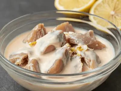 Cubed chicken folded through a pale orange yogurt marinade in a glass bowl